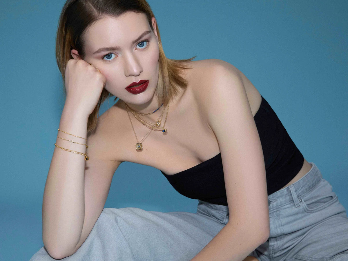 Model mit goldfarbenen Ketten, Ringen und Armbändern vor blauem Hintergrund.