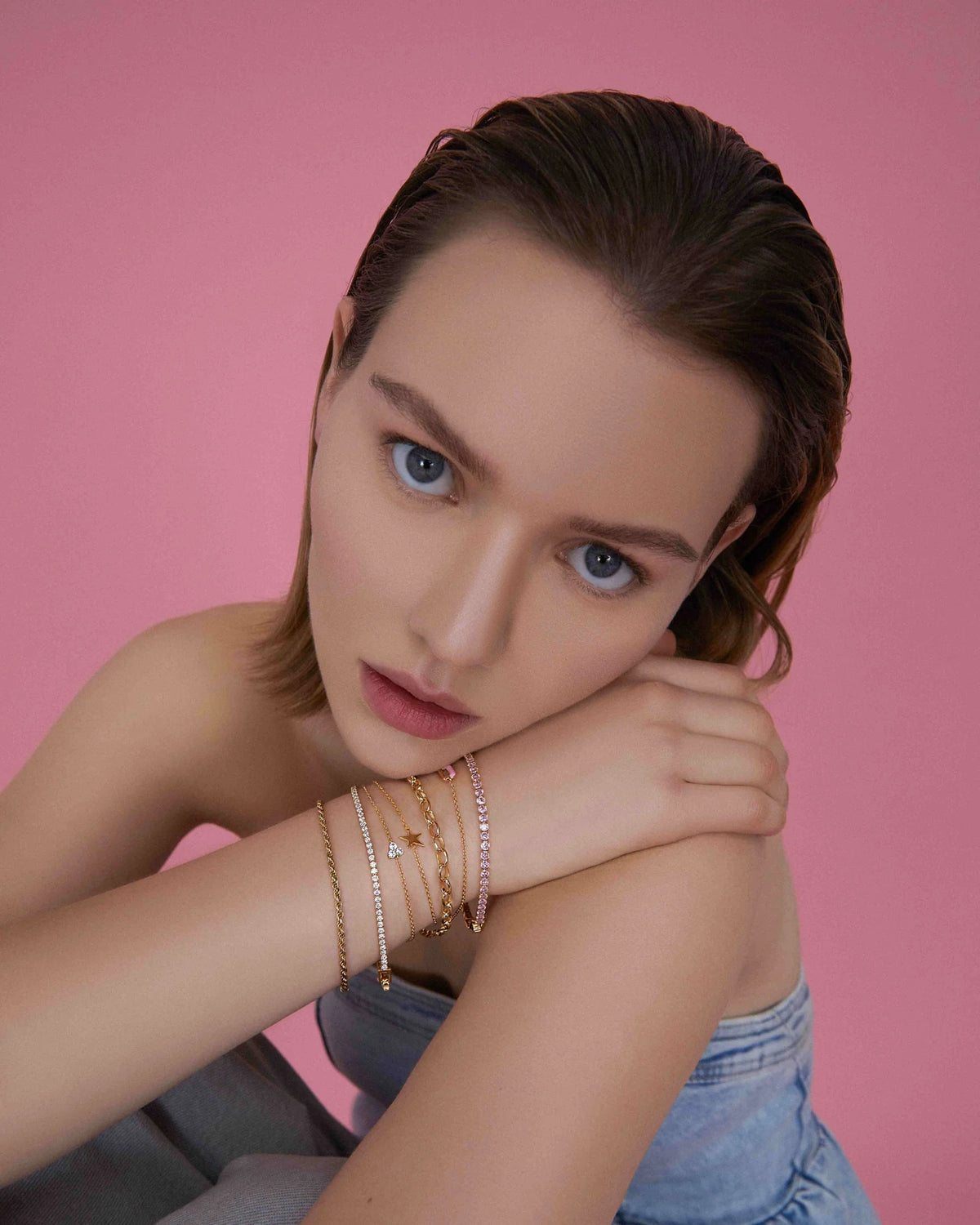 Model mit goldfarbenen Armbändern vor rosafarbenem Hintergrund.